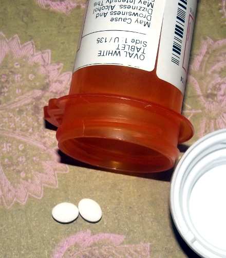 two clonidine tablets laying beside an open empty prescription bottle and lid